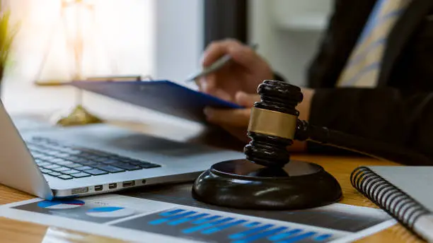 Photo of Lawyer working on papers on a table with judge's hammer and gold scales, legal concepts and consultants.