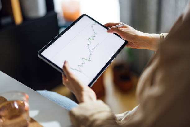 High angle view of anonymous businesswoman using digital tablet for online trading while working from home office