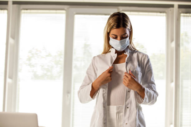 Female doctor in protective face mask buttoning her lab coat