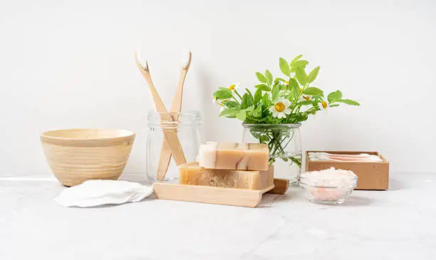 Natural bathroom and home spa tools. Zero waste sustainable lifestyle concept. Bamboo toothbrush, natural soap bar, cotton pads and swabs, flowers and brush on white background. Front view, copy space