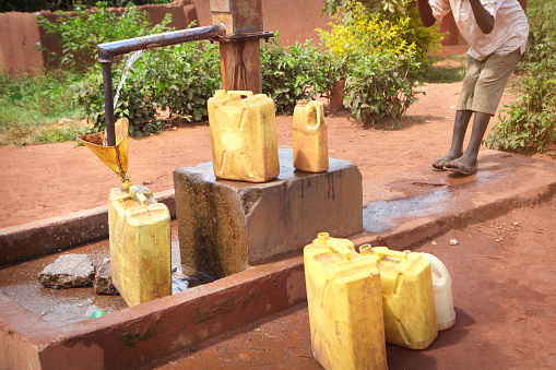 Local person pumping water into plastic canisters in african village