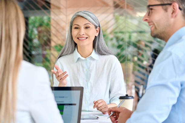 giovane donna d'affari asiatica matura e matura che forma giovani tirocinanti stagisti spiegando la condivisione di competenze professionali durante la riunione di gruppo in un ufficio moderno. insegnante di mezza età con gruppo di studenti in seminario. - mature student learning training computer foto e immagini stock