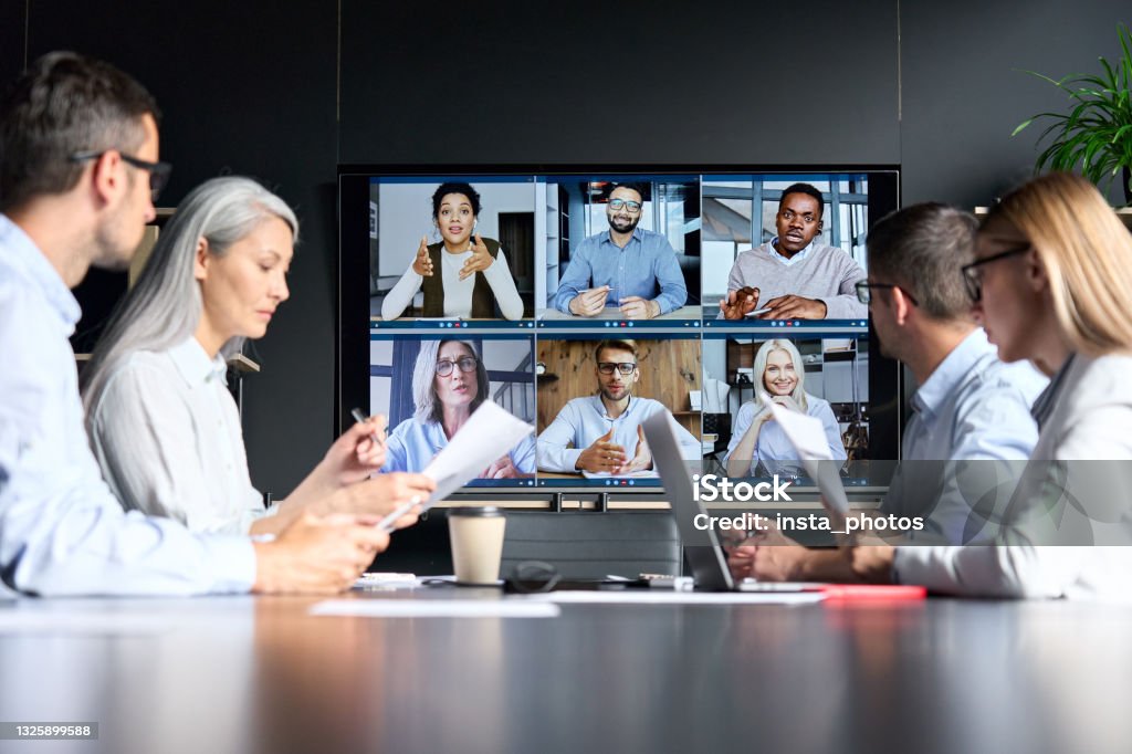 Global corporation online videoconference in meeting room with diverse people sitting in modern office and multicultural multiethnic colleagues on big screen monitor. Business technologies concept. Meeting Stock Photo