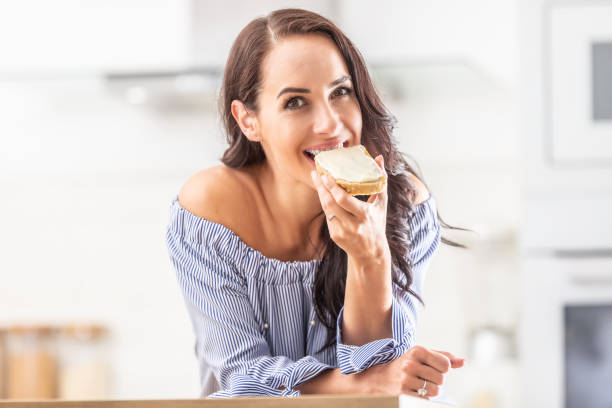 Good-looking girl bites off the slice of bread with a white spread.