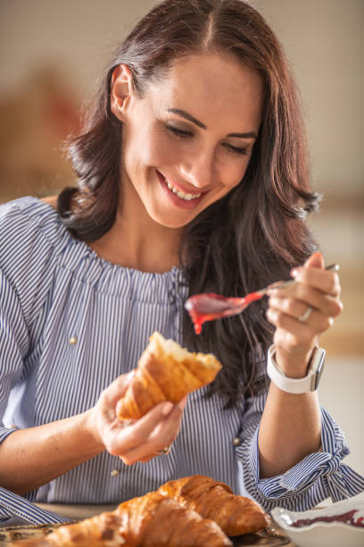 la donna sorride mentre ama la colazione con croissant e marmellata. - preserves croissant breakfast food foto e immagini stock