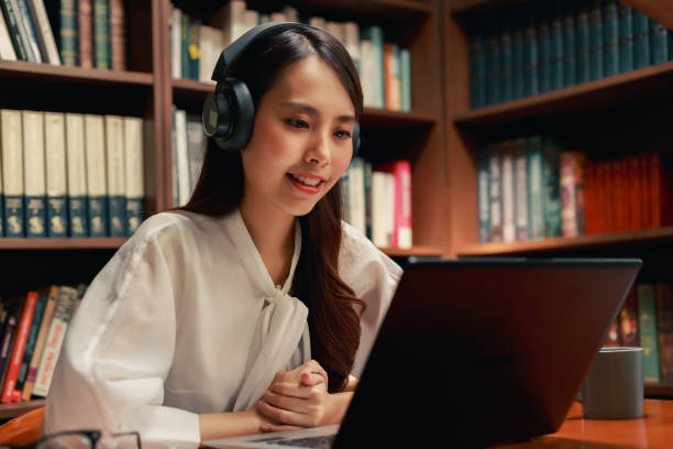 istock attractive asian woman using laptop computer and headphone making video conference in the reading room. 1325903220