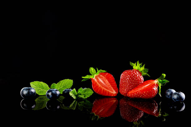istock Strawberries and blueberries with mint leafs on the black glass background with a reflection. Selective focus. 1325905783