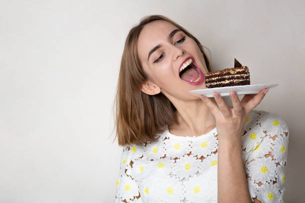 Pleased girl bites yummy cake Pleased woman bites tasty chocolate cake over a grey background. Empty space cake models stock pictures, royalty-free photos & images