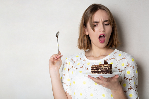 Young displeased surprised woman looking to the sweet cake with cream. Empty space