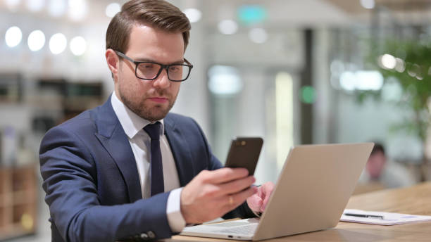 istock Young Businessman using Smartphone and Laptop at Work 1325906018