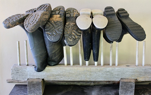 Horizontal close up still life of farm rubber muddy gumboots upside down to avoid spiders on hand made wood holder at a country estate