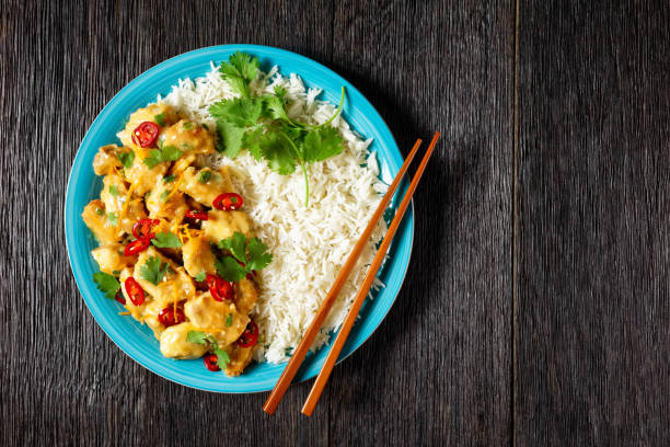 istock Mango glazed spicy chicken breast chunks with rice on a blue plate with chopsticks, on a dark wooden table, horizontal view from above, flat lay, free space 1325906992