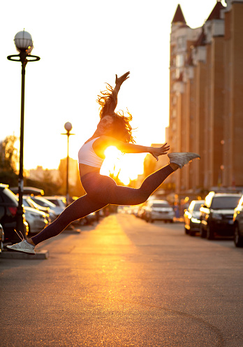 Athletic dancer woman jumping at the street in gold evening sun light