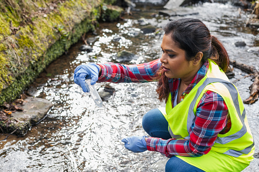 A female scientist collects and looks at samples of water from a stream in Hexham and is analyzing the sample for traces of pollutants and also for traces of small microplastics before taking it back to the lab to test further.