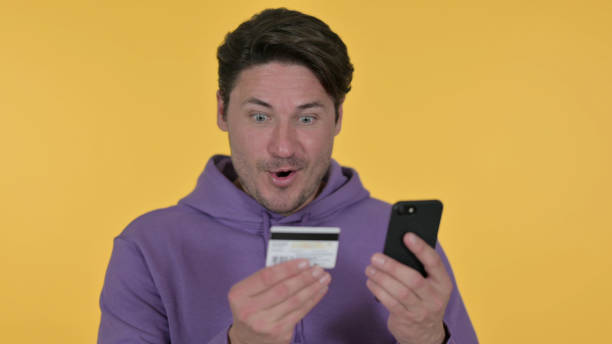 istock Middle Aged Man Doing Online Shopping on Phone, Yellow Background 1325913289