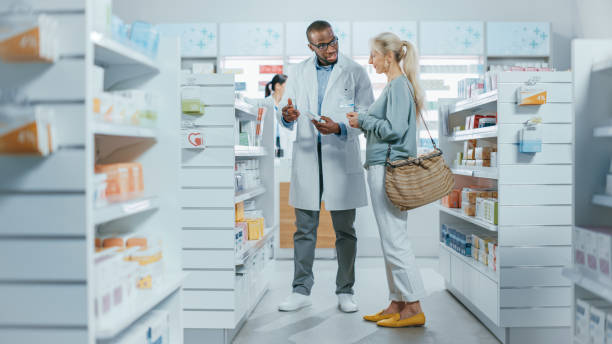 Pharmacy: Professional Black Pharmacist Helping Caucasian Senior Female Customer with Medicine Recommendation, Advice, Talking. Cusotmer Support in Drugstore Full of Drugs, Pills, Health Care Products farmacia: farmacéutico negro profesional que ayuda al cliente femenino mayor caucásico con la recomendación de la medicina, consejo, hablando. apoyo cusotmer en la farmacia llena de medicamentos, píldoras, productos de cuidado de la salud