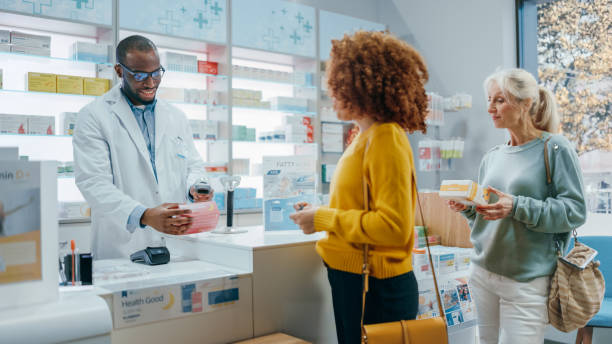 pharmacy drugstore checkout counter: professional black pharmacist provides best customer service to diverse group of multi-ethnic clients buying medicine paying with contactless payment credit cards - multi vitamine stockfoto's en -beelden