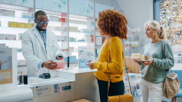 pharmacy drugstore checkout counter: professional black pharmacist provides best customer service to diverse group of multi-ethnic clients buying medicine paying with contactless payment credit cards - sales clerk imagens e fotografias de stock