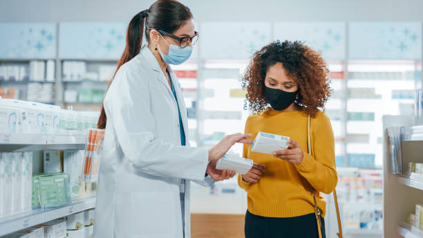 farmacia covid-19 che indossa maschere facciali: farmacista professionista che aiuta un bellissimo cliente femminile con raccomandazione di medicina, parlando. farmacia piena di farmaci, pillole, assistenza sanitaria, prodotti di bellezza - retail shopping talking customer foto e immagini stock