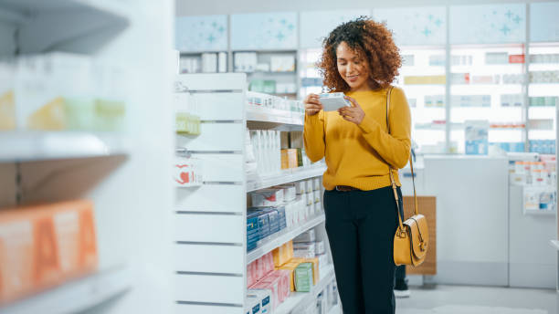 pharmacie pharmacie: belle jeune femme noire marchant entre les allées et les étagères shopping pour les médicaments, médicaments, vitamines, suppléments, produits de beauté de soins de santé avec conception d’emballage moderne - pharmacy photos et images de collection