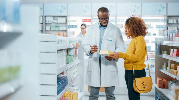 pharmacy: professional black pharmacist helping beautiful latin female customer with medicine recommendation, advice, talking. drugstore with full of drugs, pills, health care, beauty product packages - friendly match imagens e fotografias de stock