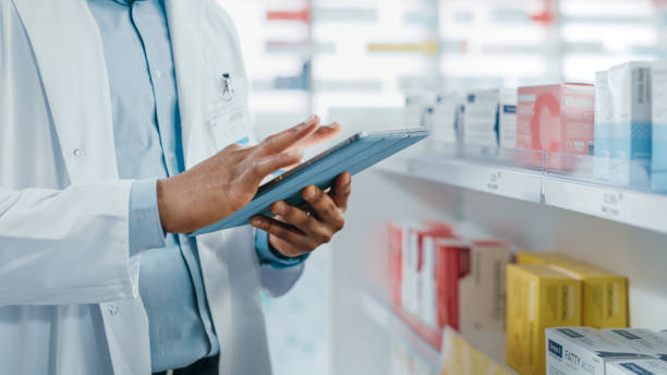 pharmacy: portrait of professional black pharmacist uses digital tablet computer, checks inventory of medicine, drugs, vitamins, health care products. druggist in drugstore store. focus on hands - pharmacist pharmacy pill medicine imagens e fotografias de stock