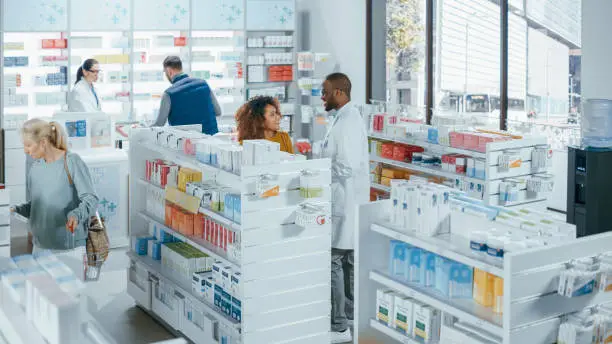 Photo of Pharmacy Drugstore: Diverse Group of Multi-Ethnic Customers Browsing Shelves, Purchasing Medicine, Drugs, Vitamins, Supplements, Health Care Products from Professional Pharmacist at Cashier Counter