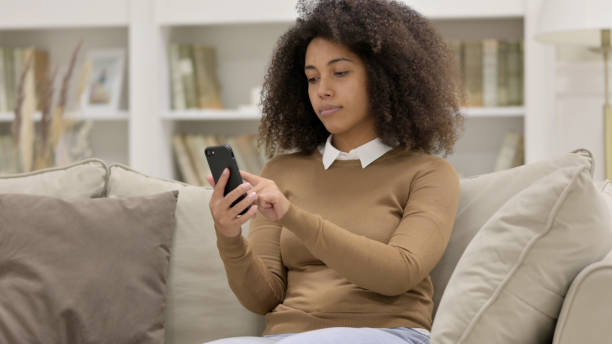 istock Young African Woman Using Smartphone on Sofa 1325915768