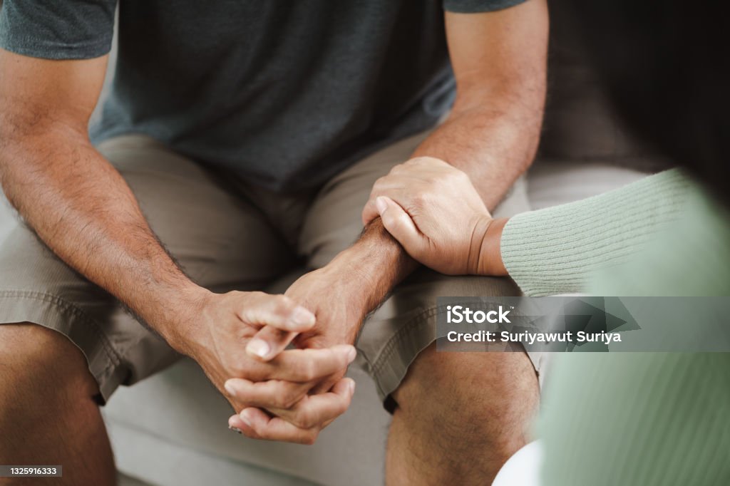 Female friend or family sitting and hold hands during cheer up to mental depress man, Psychologist provides mental aid to patient. PTSD Mental health concept. Mental Health Stock Photo