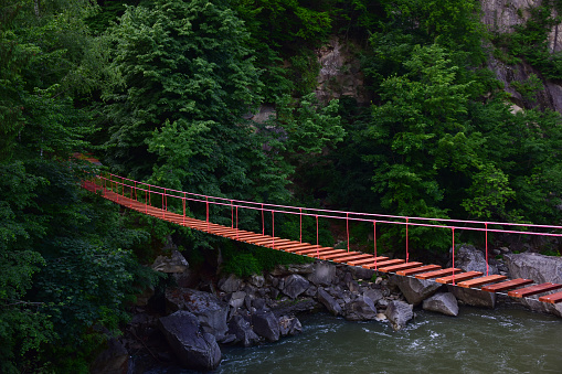 Suspended rope bridge without people with rocky banks over a mountain river against a background of a mountain in lush green vegetation