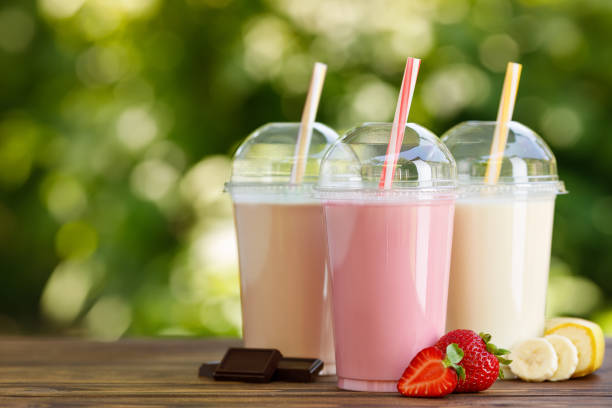 set of different milkshakes in disposable plastic glasses set of different milkshakes in disposable plastic glasses on wooden table outdoors smoothie stock pictures, royalty-free photos & images