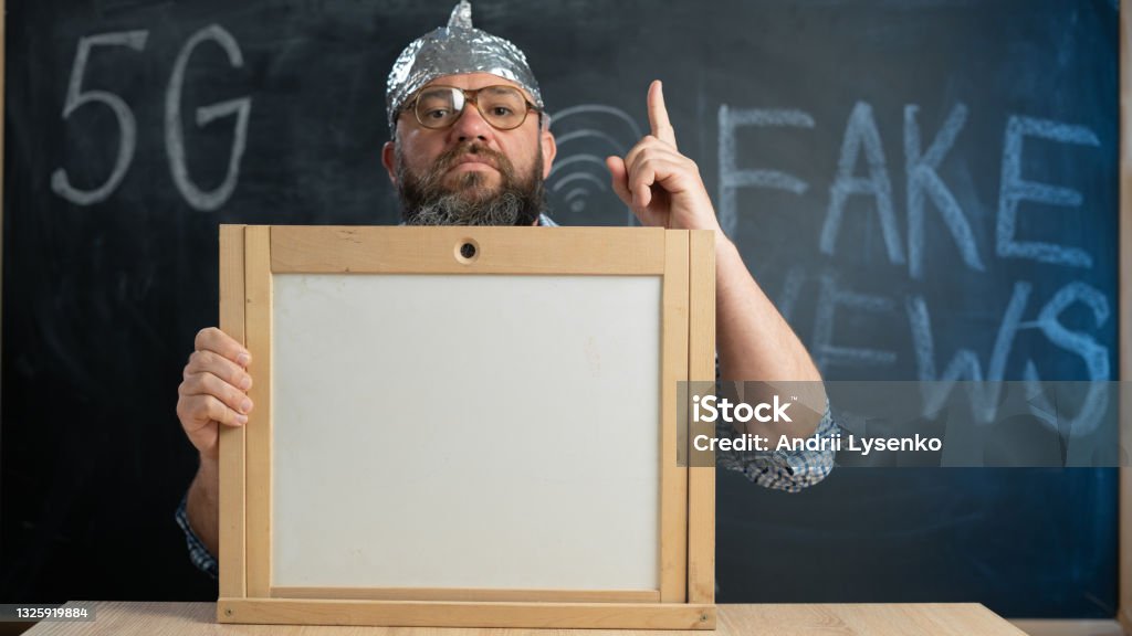 stupid conspiracy theory guy in a foil hat holds a blackboard with space for text. A bearded conspiracy theorist. Total control and fake news. Conspiracy and 5g. Mind control. stupid conspiracy theory guy in a foil hat holds a blackboard with space for text. A bearded conspiracy theorist. Total control and fake news. Conspiracy and 5g. Mind control. Thumbs up onto the board Foil - Material Stock Photo