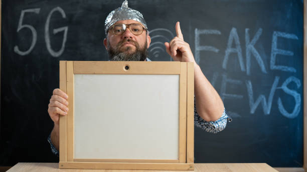 stupid conspiracy theory guy in a foil hat holds a blackboard with space for text. A bearded conspiracy theorist. Total control and fake news. Conspiracy and 5g. Mind control. stupid conspiracy theory guy in a foil hat holds a blackboard with space for text. A bearded conspiracy theorist. Total control and fake news. Conspiracy and 5g. Mind control. Thumbs up onto the board tin foil hat stock pictures, royalty-free photos & images