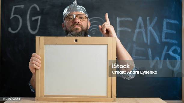 Stupid Conspiracy Theory Guy In A Foil Hat Holds A Blackboard With Space For Text A Bearded Conspiracy Theorist Total Control And Fake News Conspiracy And 5g Mind Control Stock Photo - Download Image Now