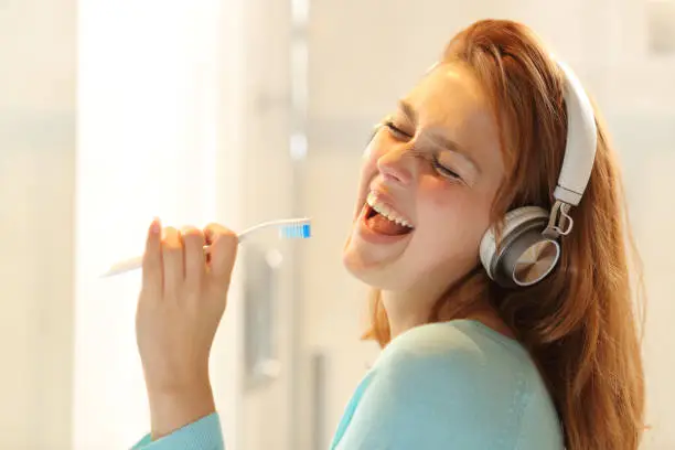 Photo of Happy lady listening to music and singing with a toothbrush