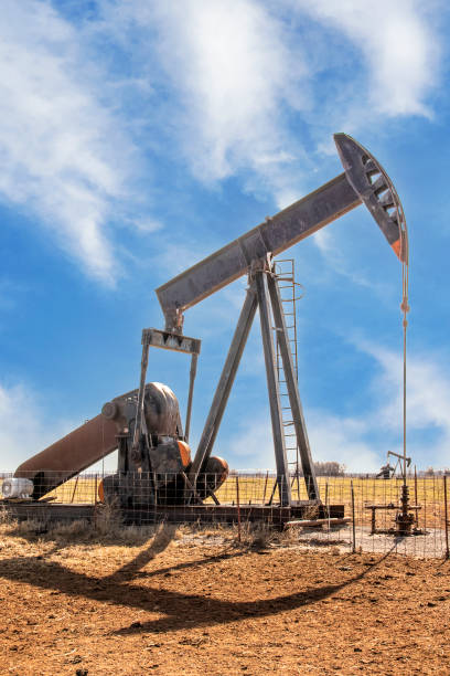 Oilfield pump jack out in summer red dirt field on bright day with shadow and a few whispy clouds in blue sky stock photo
