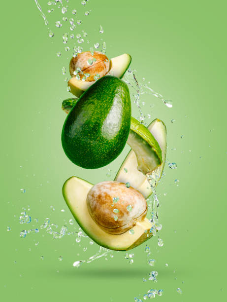 Fresh avocado cut into slices with water drops splash flying in the air and levitate on a mint green background. Healthy diet ingredient recipe. Trendy motion food composition. Creative fruit concept. aguacate fresco cortado en rodajas con gotas de agua salpican volando en el aire y levitan sobre un fondo verde menta. receta de ingredientes de dieta saludable. composición de alimentos de movimiento de moda. concepto creativo de la fruta.
