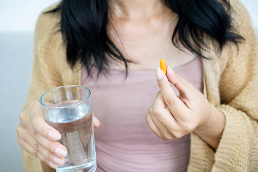 woman hand taking turmeric pill, girl hand holding turmeric powder in capsule or curcumin herb medicine with a glass of water, treatment for acid reflux problem