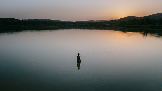 Aerial view photo of a young woman enjoying summer sunset on the lake