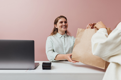 Clothing store owner giving a shopping bag to customer. Unrecognizable woman buying clothes in a fashion shop.