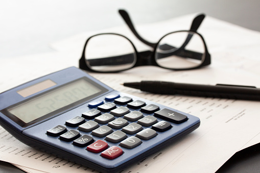 Calculator, glasses, pen and papers on white fading background with copy space. Business concept.