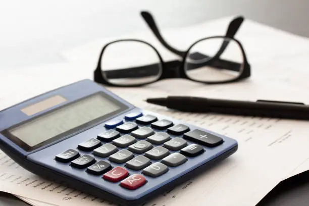 Photo of Calculator, glasses, pen and papers on white fading background with copy space.