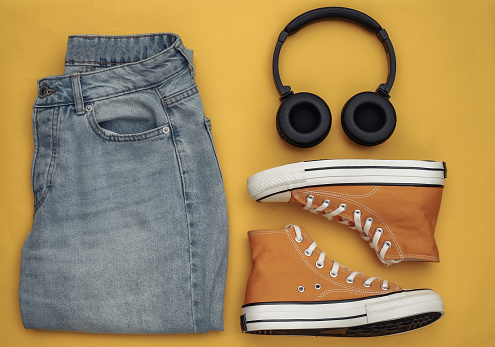 Youth clothing and accessories. Sneakers, jeans and headphones on a yellow background. Top view. Flat lay