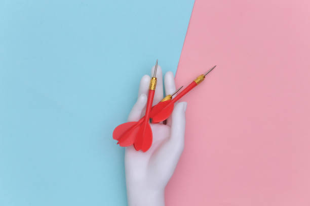 istock White mannequin hand holds dart needle on pink blue pastel background. Top view 1325932886