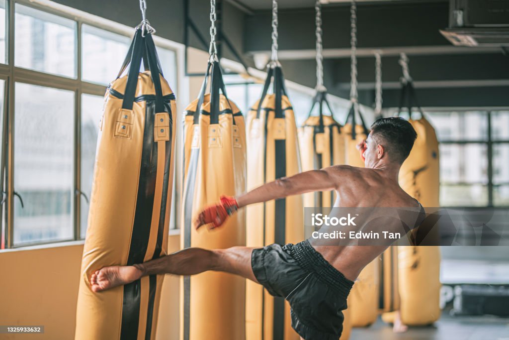 asian malay muay thai boxing boxer kick punching bags in gym health club asian malay muay thai boxer flying kick punching bags in gym health club Muay Thai Stock Photo