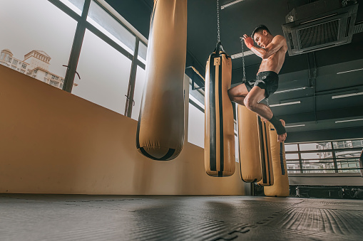 asian malay muay thai boxing boxer flying kick punching bags in gym health club