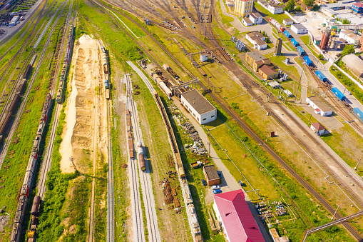 railway tracks with freight trains, a locomotive with cars passing in the background. View from drone.