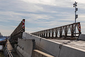 Road across an iron makeshift bridge built over the Nove Mlyny reservoir in the Czech Republic. Marking of limited speed and narrowing of the road. The background is a blue sky with white clouds