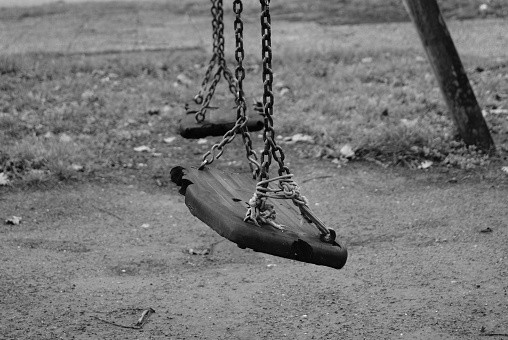 Black and white photo of an old abandoned playground. Melancholy childhood memories. Seats hung with chains ruined by time.