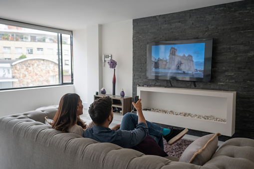 Happy Latin American couple relaxing at home watching a movie on the tv in the living room - lifestyle concepts. **IMAGE ON SCREEN BELONGS TO US**